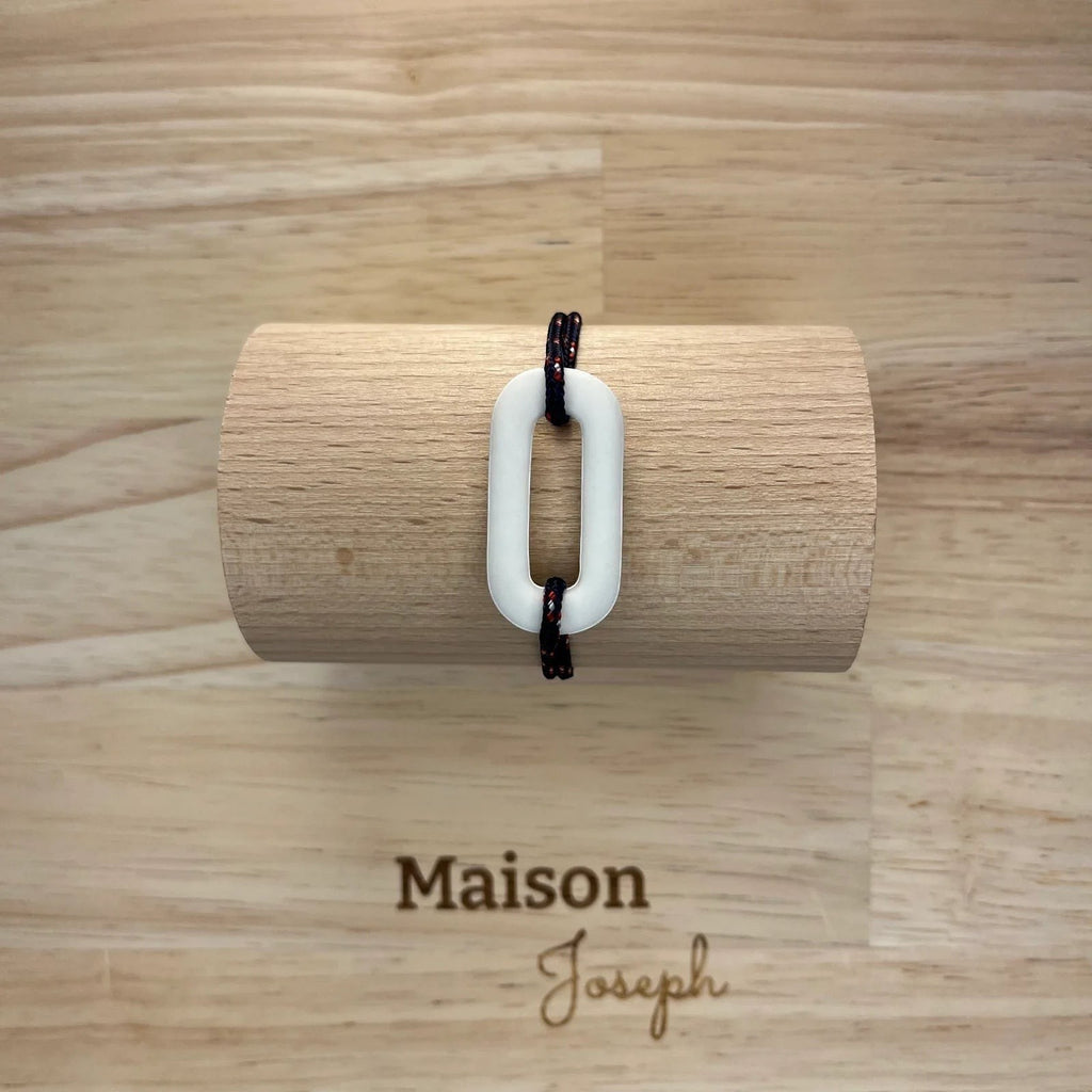 Bracelet O de Océan Maison Joseph en céramique blanche sur cordon marin sport réglable, présenté sur support bois.